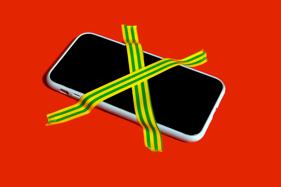 White smartphone with a black screen bound by neon yellow-green striped tape crossing over it on a bright red background.