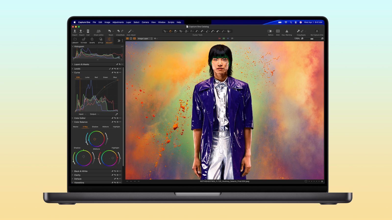 Laptop screen showing a photo-editing app with a model wearing a metallic silver outfit and a purple coat against a colorful powder-like background.