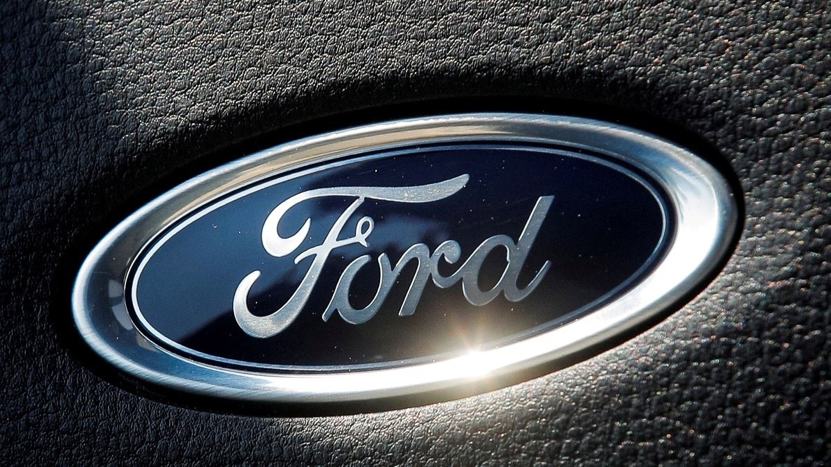 Ford logo oval emblem on a textured black surface, chrome border and sun glare highlight the brand mark on a car interior