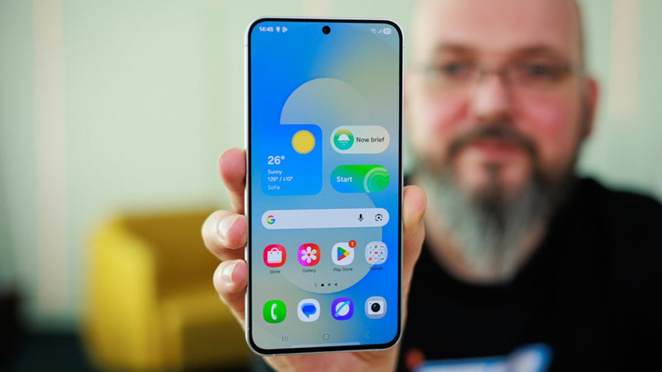 Person holding a smartphone toward the camera, displaying a colorful home screen with weather widget and app icons.