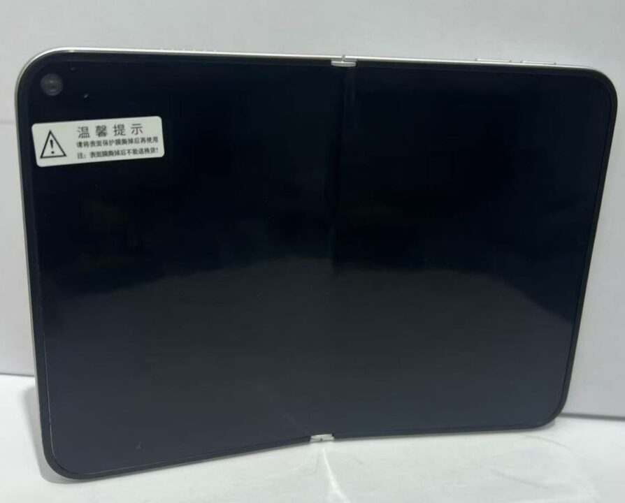 1000039873 Glossy, rounded-corner black rectangular device (likely a laptop or tablet) with a small warning sticker in the top-left corner.