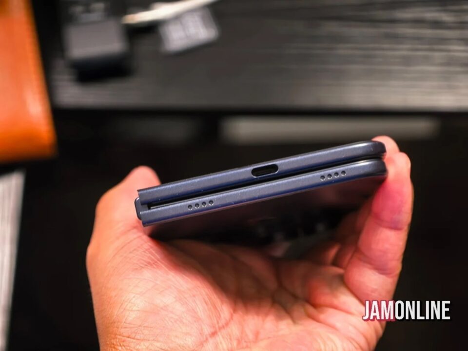 Blue foldable smartphone held in a hand, showing the USB-C charging port and speaker grills on the bottom edge.