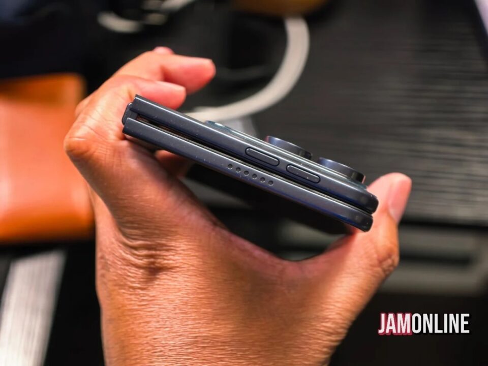 Close-up of a hand holding a dark gray foldable smartphone with side buttons and a hinge visible.