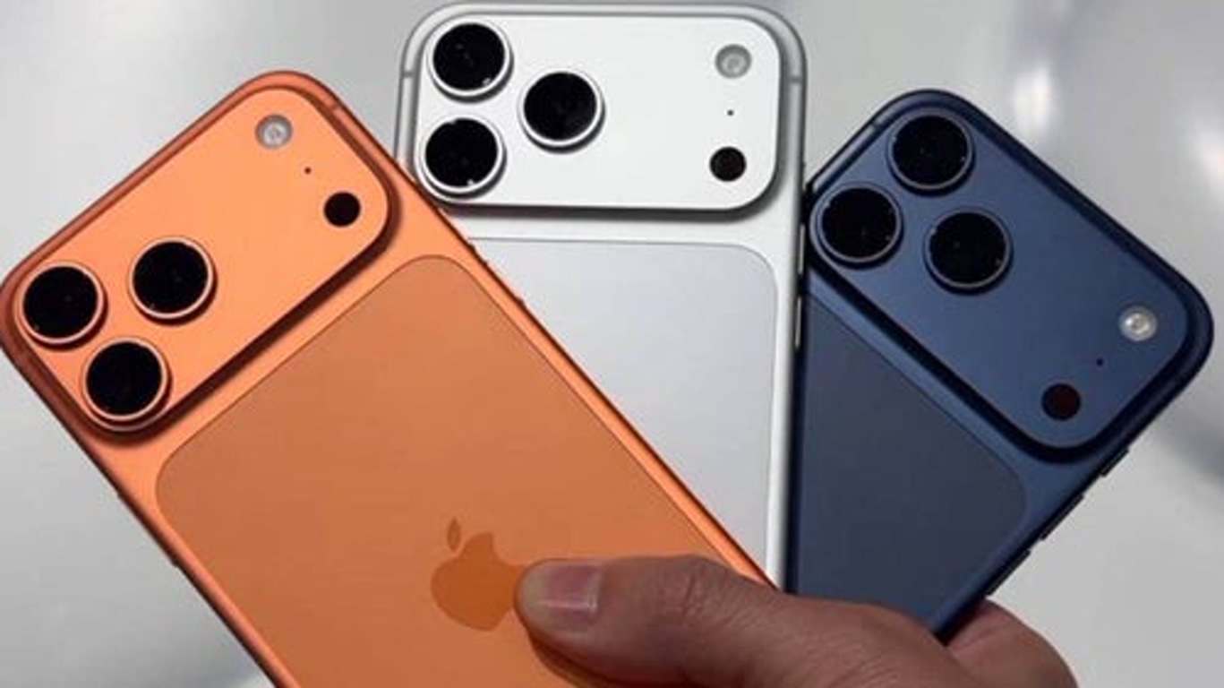 Three iPhone smartphones in orange, white, and blue colors held together, displaying their triple-camera backs with Apple logos visible.
