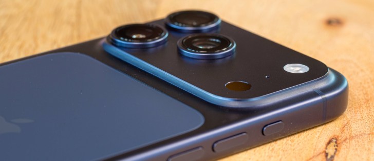 Close-up of a dark blue smartphone back with triple camera lenses on a wooden table.
