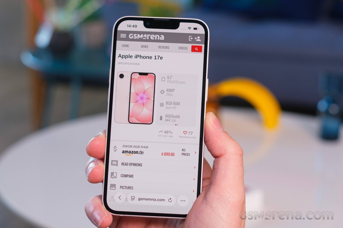 Hand holding a smartphone displaying a GSMArena product page for the Apple iPhone 17e with specs and price on screen.