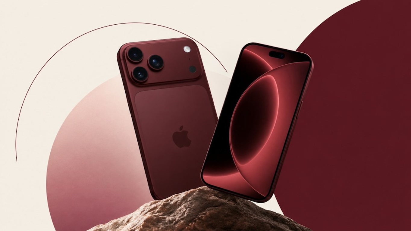 Red iPhone with a triple-camera back rests on a rocky surface, set against abstract beige and burgundy shapes.