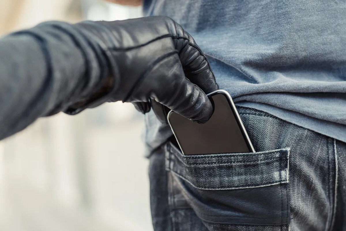 Gloved hand placing a smartphone into the back pocket of blue jeans.
