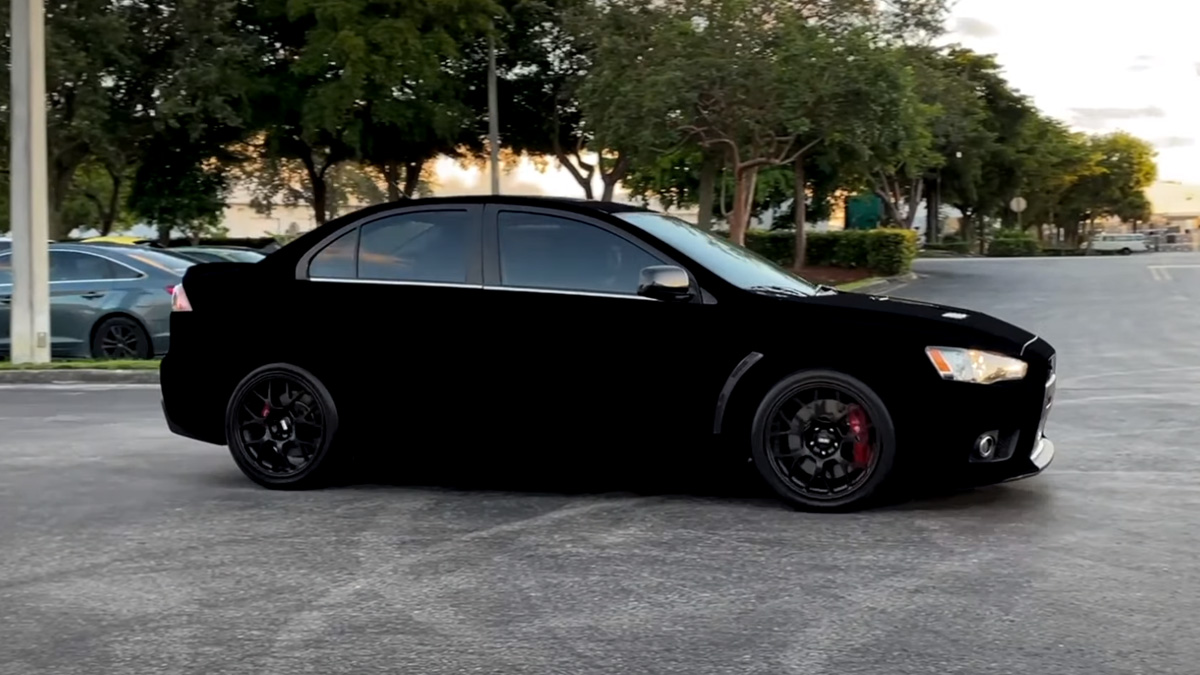 Side view of a glossy black sports sedan with dark wheels parked in a lot.