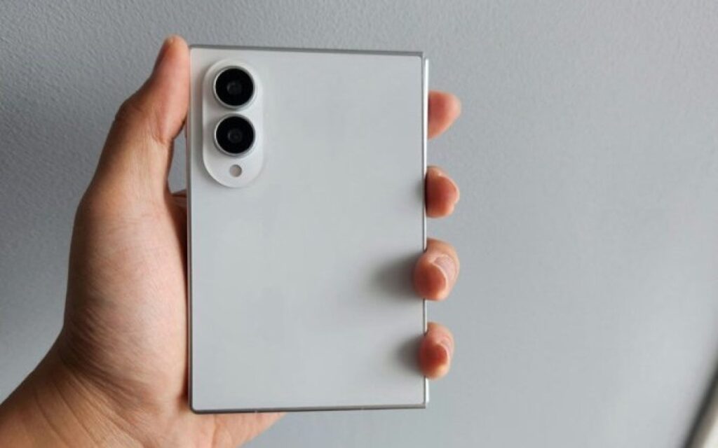 Hand holding a silver smartphone from the back, showing a twin-camera module in the top-left corner of the device.
