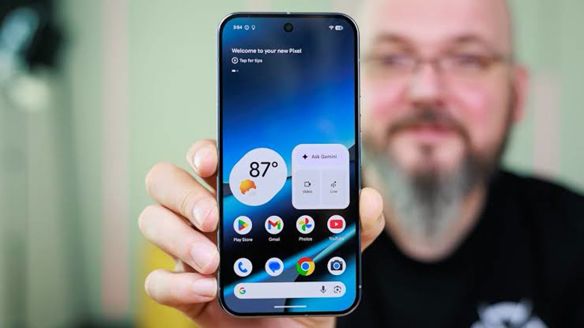 A person holds up a smartphone displaying the home screen with a weather widget showing 87° and app icons like Play Store and Gmail on the screen.