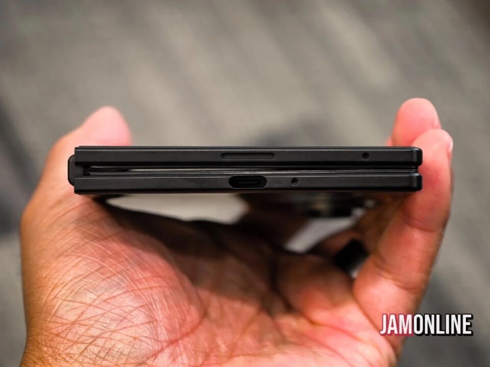 Close-up of a hand holding a thin black smartphone with dual SIM/microSD tray on the side.