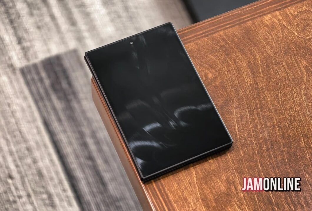 Folded black smartphone resting on a wooden table, viewed from above, with a JAMONLINE watermark in the corner.