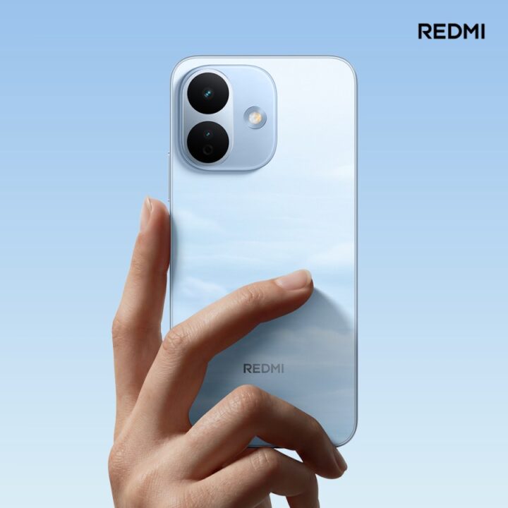 Hand holding a light blue Redmi smartphone against a gradient blue background, showcasing the rear camera module and branding on the back.