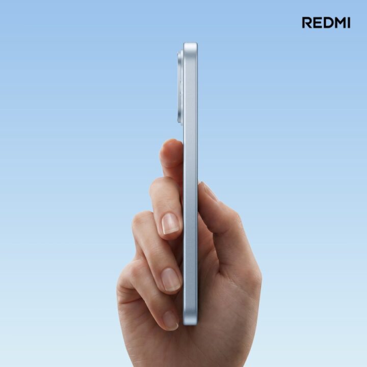 Side profile of a hand holding a slim silver Redmi smartphone against a gradient blue background.