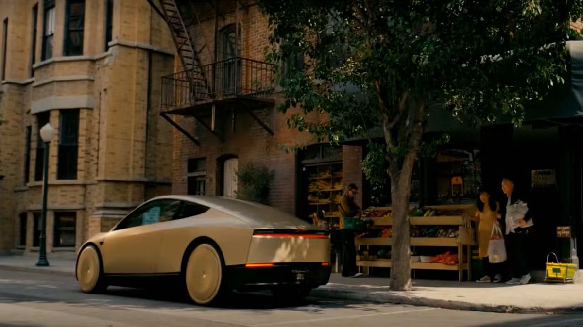 A futuristic gold car parked on a city street beside a fruit/produce stand with pedestrians nearby.