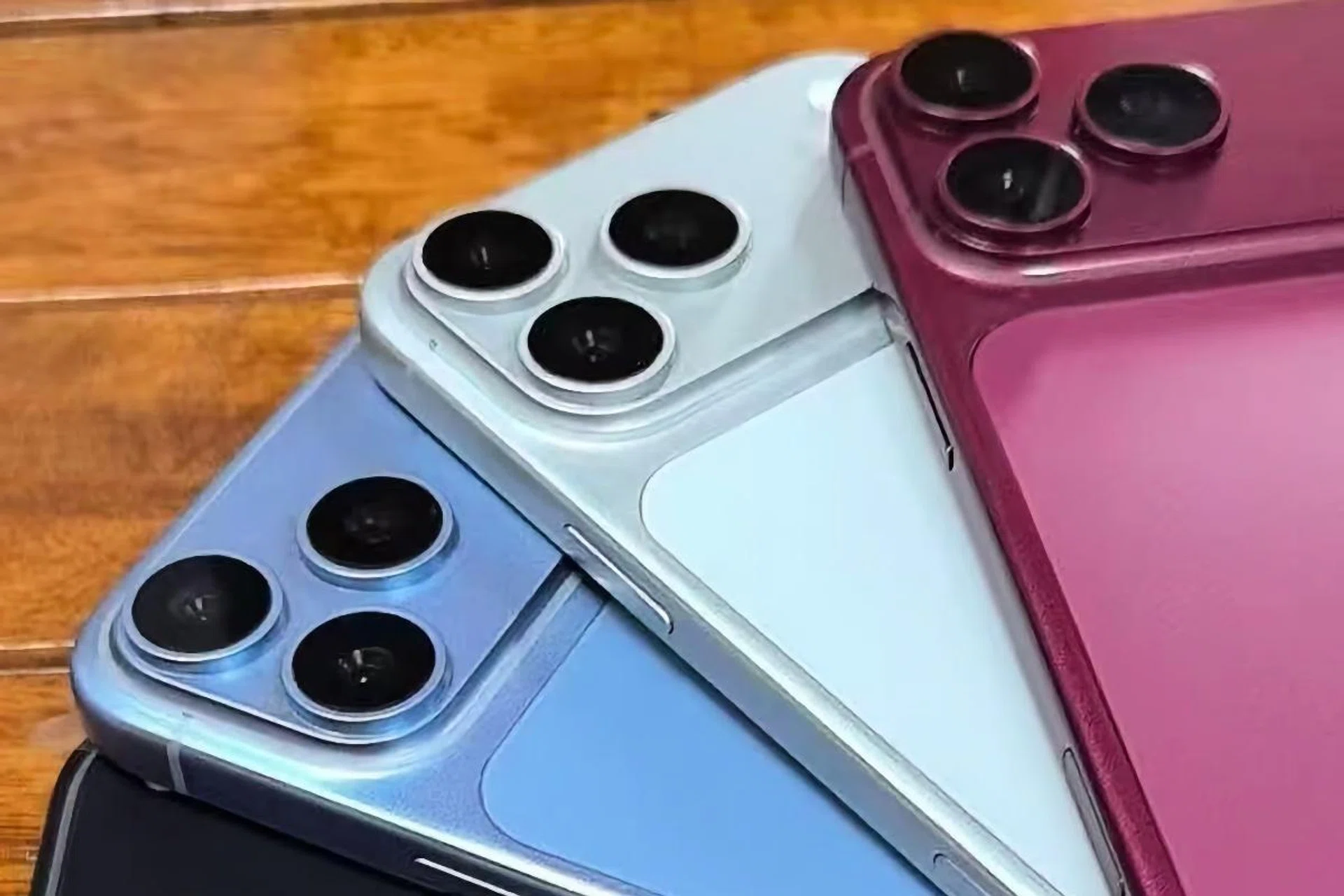 1000049380 Close-up of blue and purple iPhones with triple-camera backs on a wooden surface behind them.