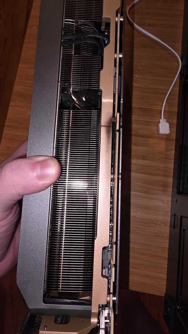 Graphics Card Viewed from the Side Showing a Metal Heatsink with Numerous Fins and a Persons Finger Holding the Edge of the Card Edge