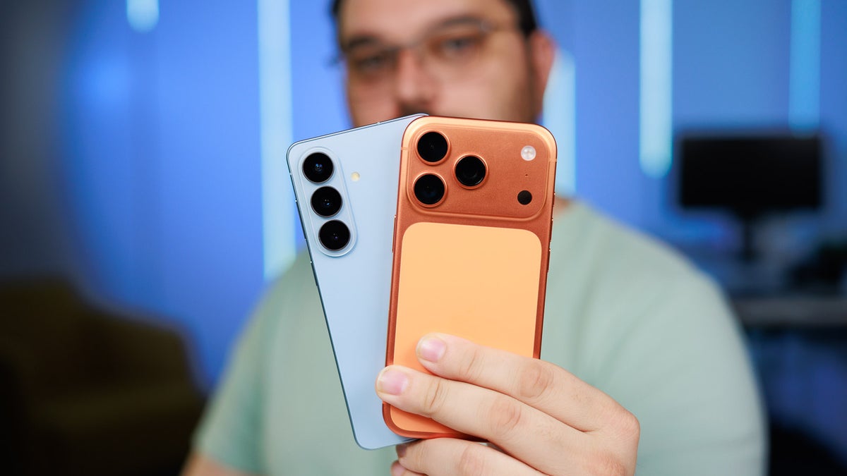 Person holding two smartphones with protective orange and blue cases, cameras facing the viewer.