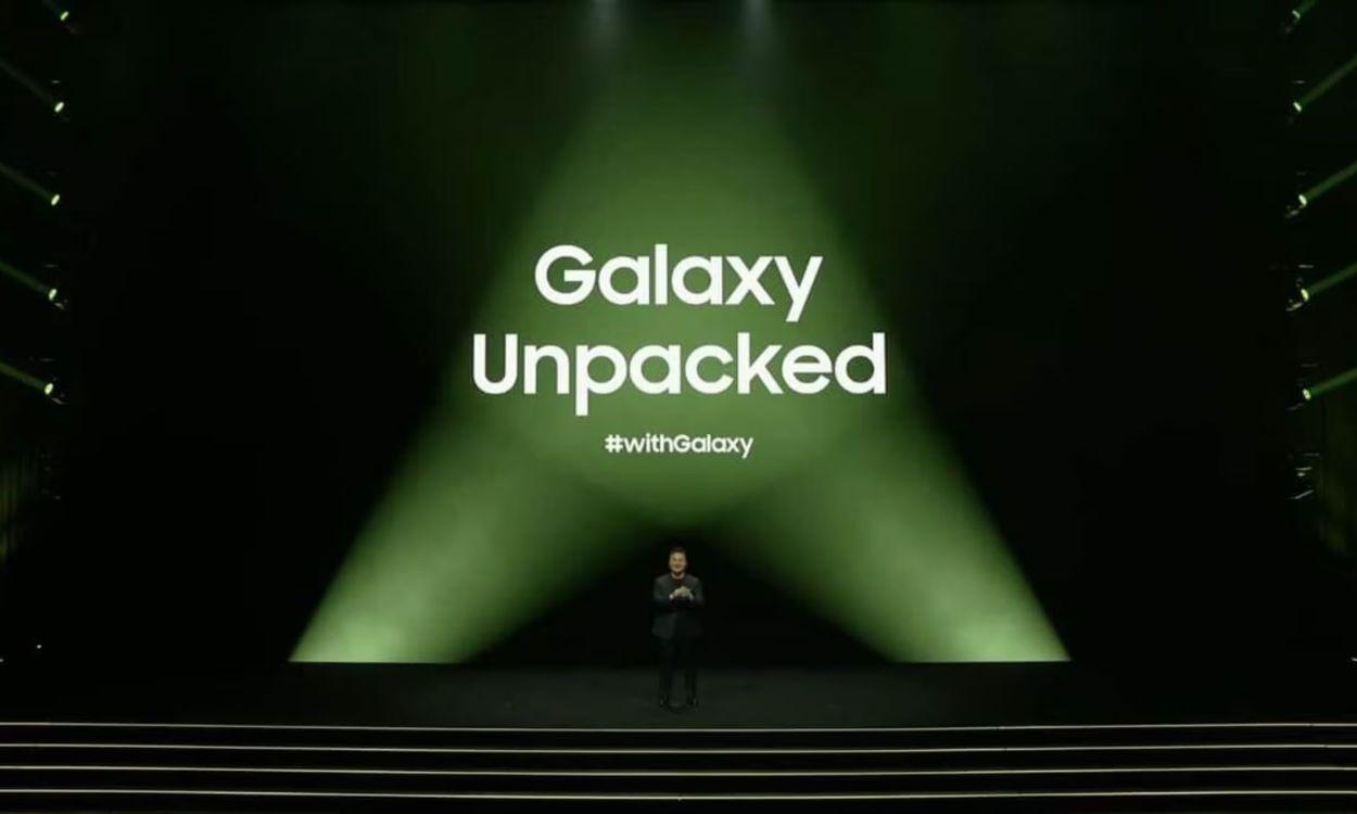 Presenter on a dark stage with a large green spotlight backdrop reading 'Galaxy Unpacked' and the hashtag '#withGalaxy' nearby, at an event.