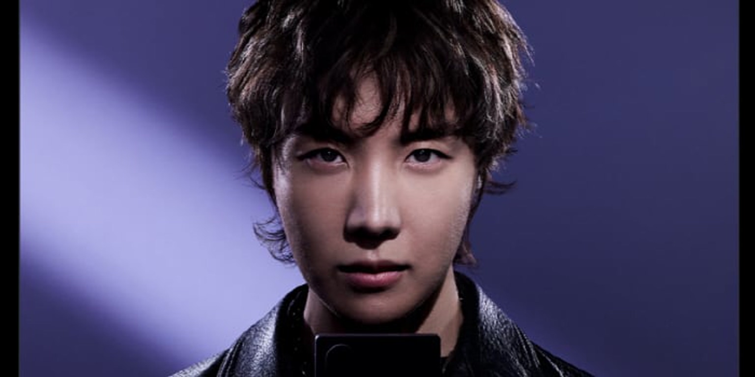Close-up portrait of a young Asian man with tousled hair wearing a black leather jacket, under purple stage lighting.