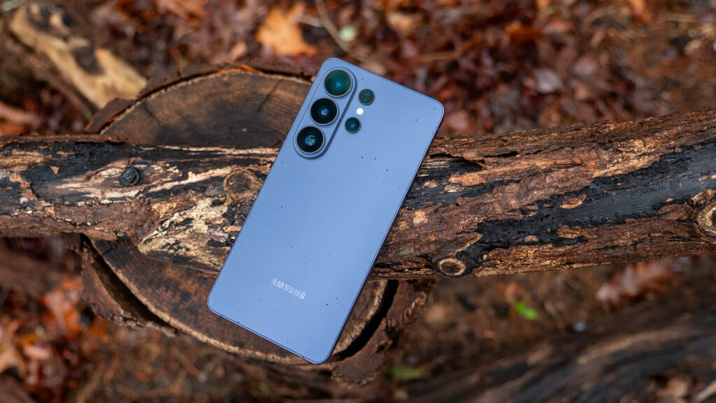 Blue Samsung smartphone resting on a rough log outdoors, camera module visible on the back.