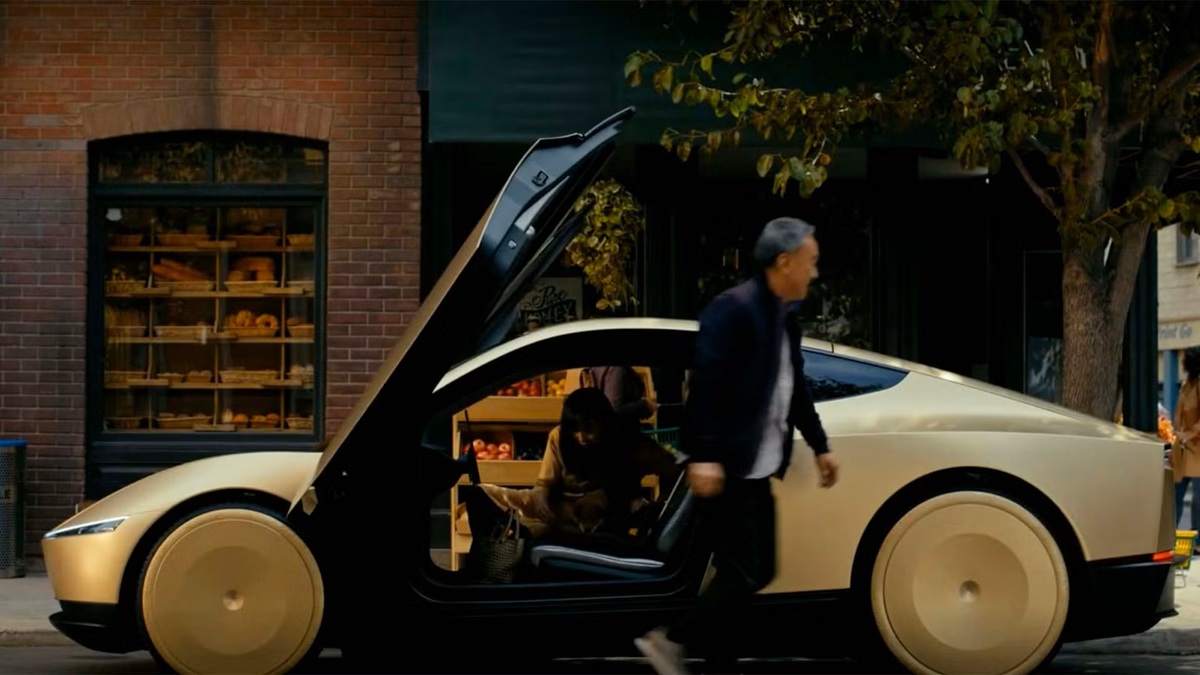 Golden futuristic sports car with upward-opening doors parked on a city street; a person sits inside near groceries while a man walks by.