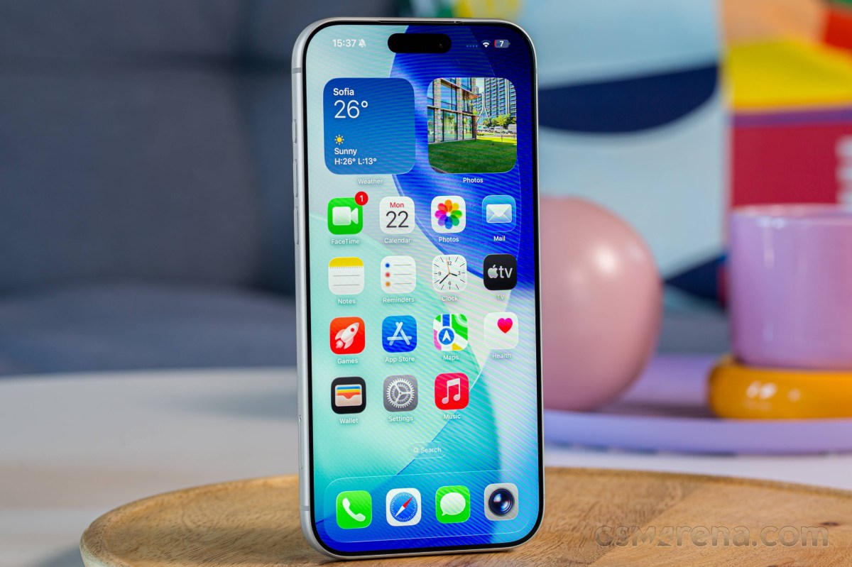 Front view of a modern smartphone standing on a wooden surface, showing a colorful home screen with app icons and widgets.