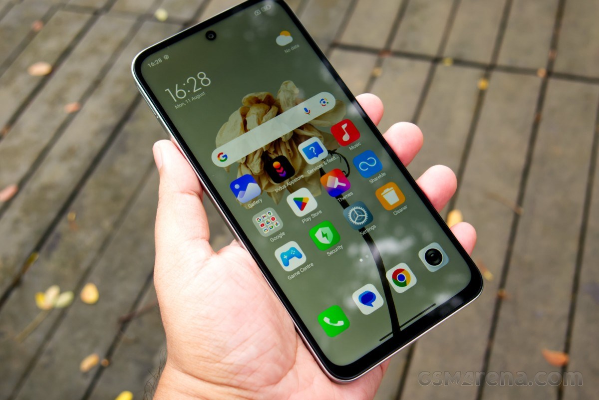 Hand holding a smartphone showing app icons on the home screen outdoors, with wooden planks in the background.