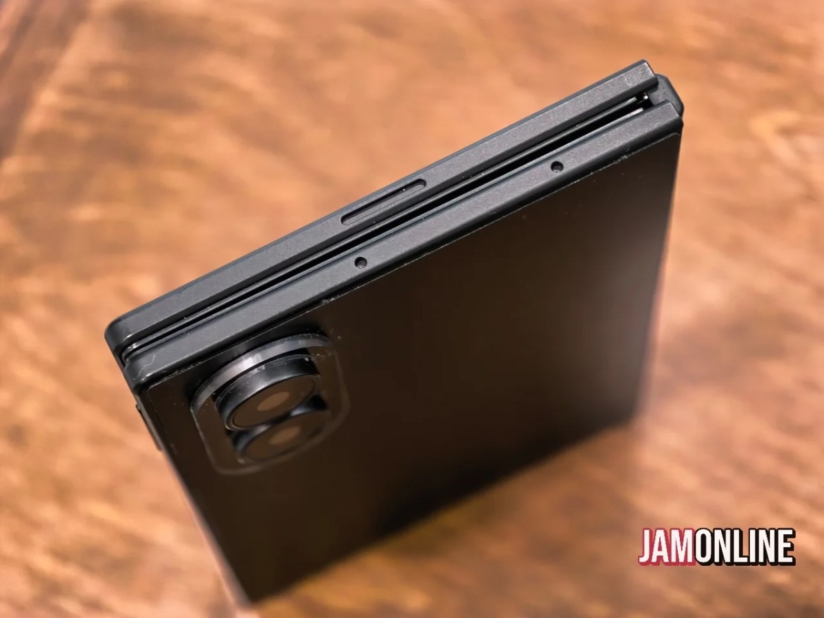 Close-up of a black smartphone showing a dual-camera module near the top edge, resting on a wooden surface.