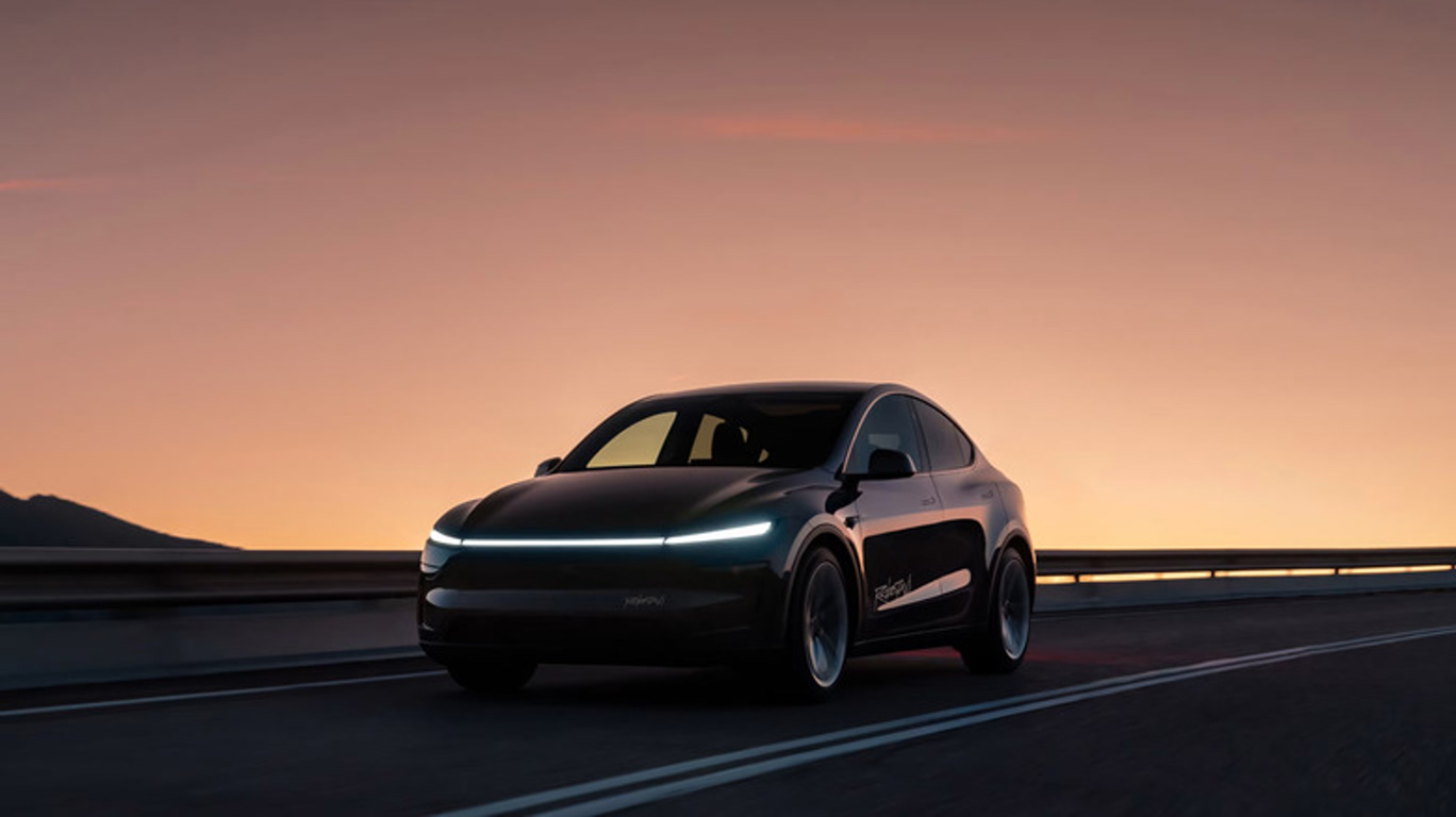 Black futuristic sedan driving on a mountain highway at sunset, with a warm orange glow on the horizon and headlights lit.