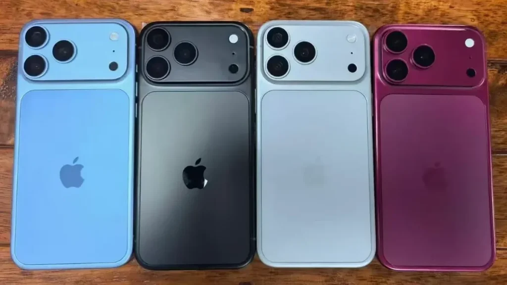 Four iPhones lined up on a wooden surface, showing rear cameras in blue, black, silver, and magenta colors.