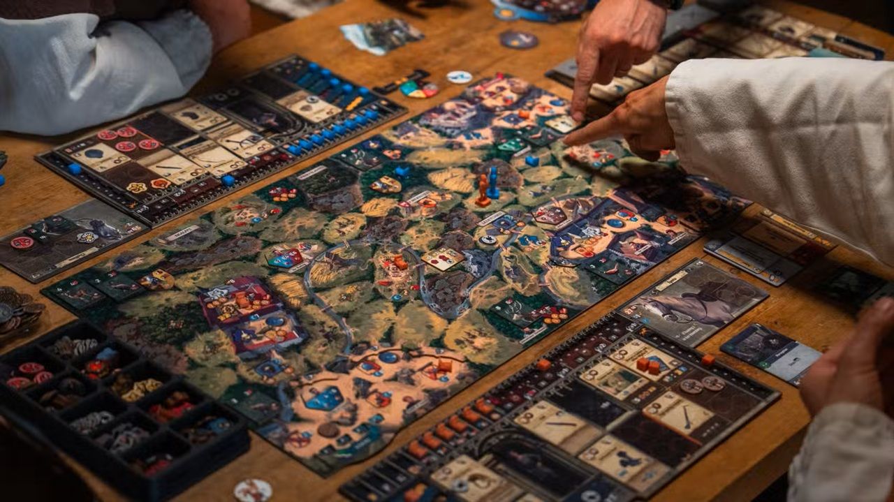 People Are Playing a Complex Fantasy themed Board Game on a Wooden Table with Map Tiles Cards and Colored Tokens in View