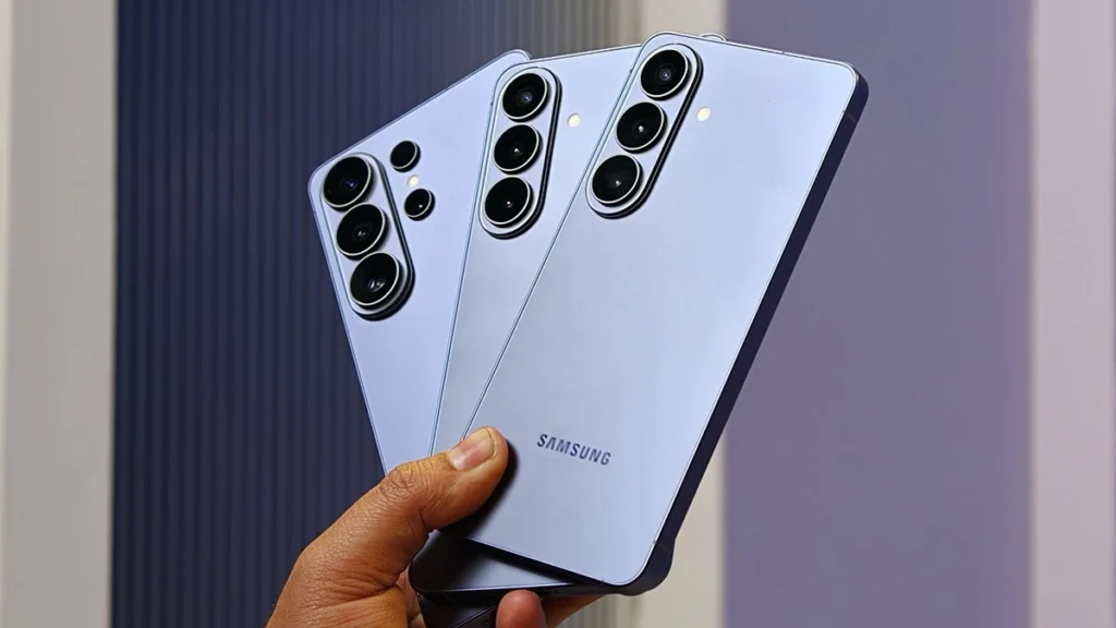 Three Samsung Galaxy smartphones with prominent rear camera modules held in a hand, fanned out for display (silver/blue finish).