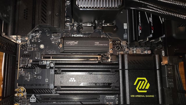 Inside a Desktop Pc Motherboard with Pcie Slots and Components Crucial Nvme Ssd Module Ram Sticks Nearby and an Msi Arsenal Gaming Logo on a Heatsinkcover