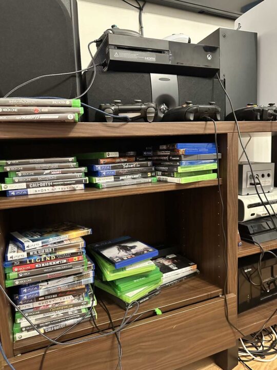 Hmkfzvaayaa0lpp min Gaming Setup on a Wooden Shelf with Two Consoles Several Controllers and Stacked Xbox and Playstation Game Cases Along the Shelves