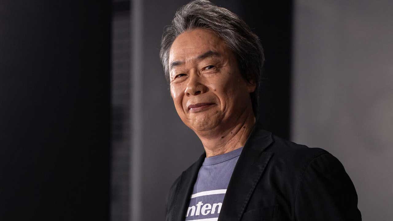 Portrait of an Older Asian Man with Gray Hair Wearing a Black Blazer and a Blue Nintendo Shirt Against a Neutral Background