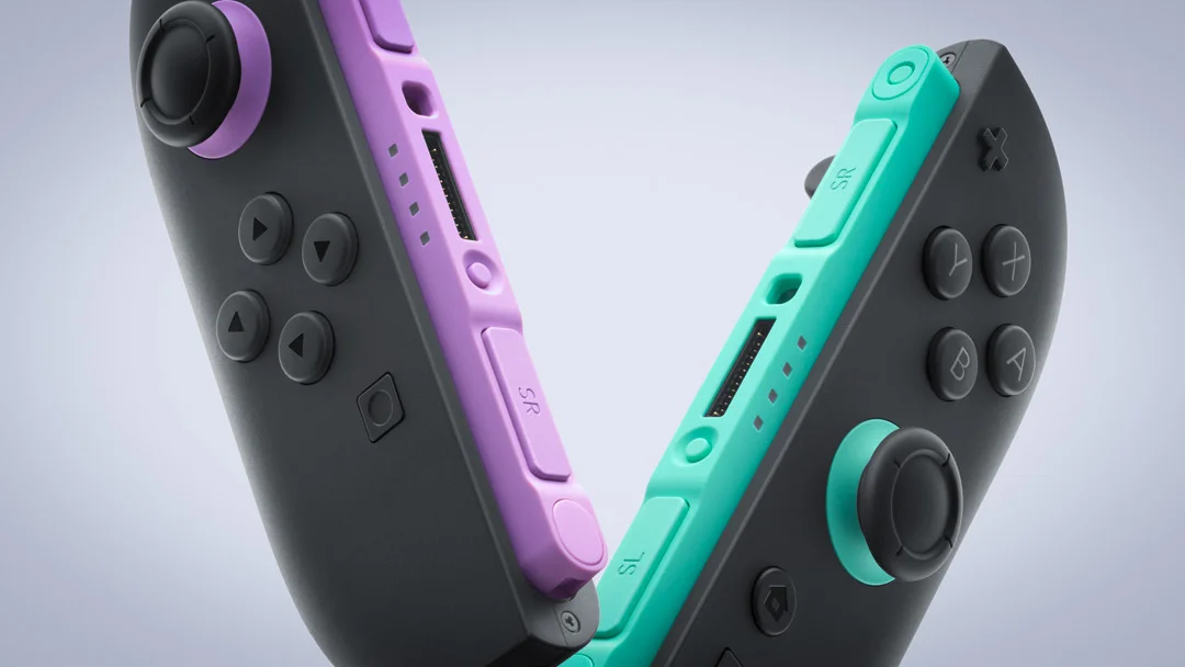 Two Joy con Controllers in Purple and Teal Leaning Against a Gray Console Showing Thumbsticks and the Abxy Buttons
