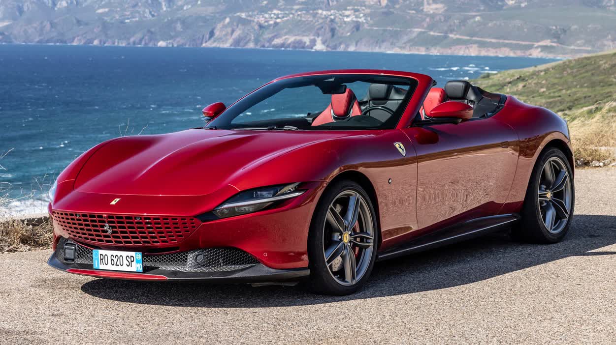 1000042759 Red Ferrari Portofino convertible parked on a coastal road with the sea and cliffs in the background, open-top luxury sports car