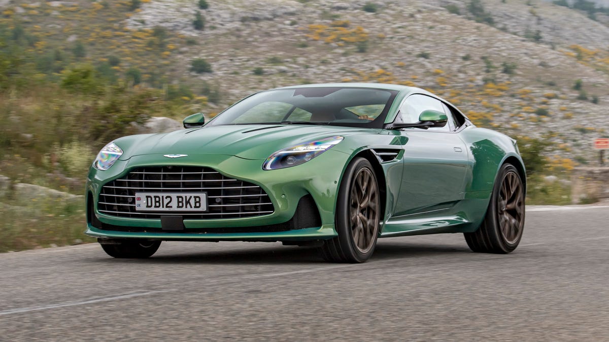 1000042743 Green Aston Martin on a winding mountain road, front 3/4 view showcasing the grille and sporty design